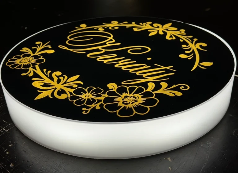 Runder Leuchtkasten in Schwarz mit goldenem Blumenmuster und eleganter Aufschrift.