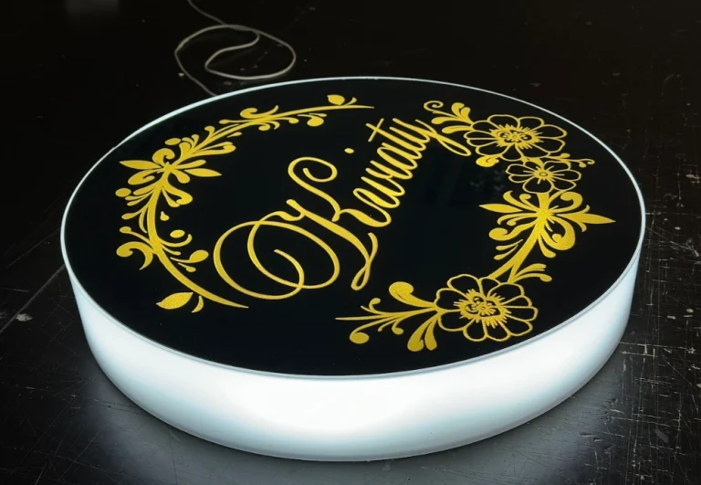 Runder Leuchtkasten in Schwarz mit goldenem Blumenmuster und eleganter Aufschrift.