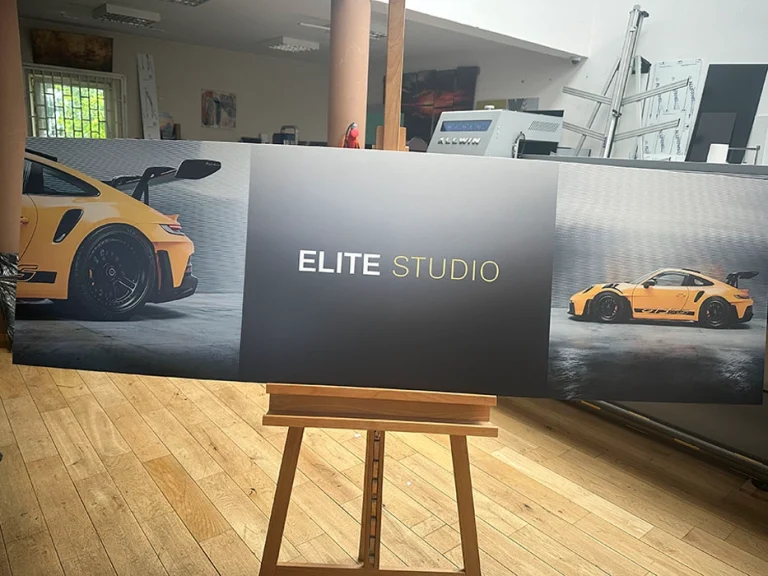 Werbeschild aus PVC mit gelbem Sportwagen und Schriftzug Elite Studio